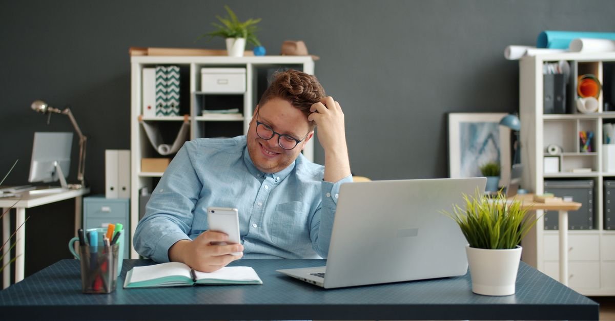 Business owner reacting with concern while checking customer reviews on his phone at his desk