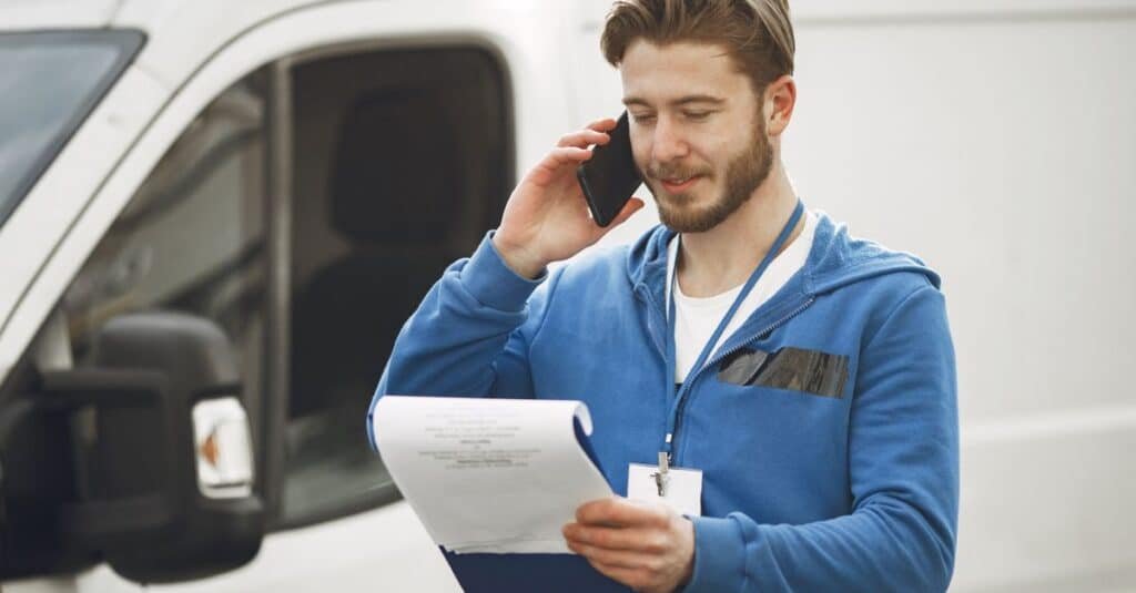 Local Services Ads Just Changed: What to Fix Now 12 Field technician answering a phone call by his service van, representing a Local Services Ads lead call for a home service businessA delivery man in a blue hoodie makes a phone call while holding a clipboard, standing by a white van.