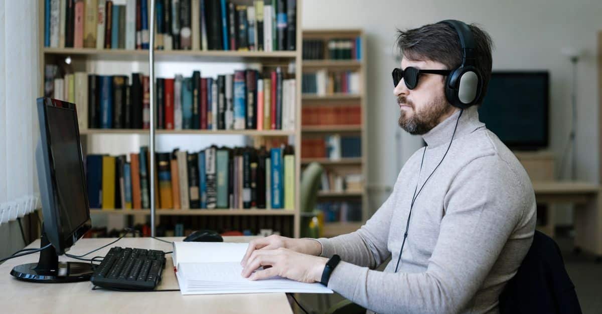 Blind man using a screen reader and braille display alongside his computer to navigate a website, illustrating ADA website compliance and accessibility for people with disabilities
