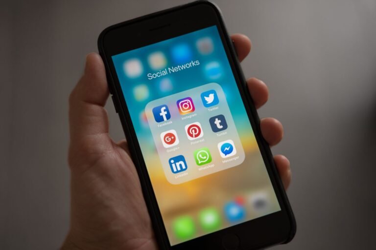 Blog 95 Hand holding a smartphone with connected social media app icons, illustrating GBP social media updates linking accounts to a Google Business Profile